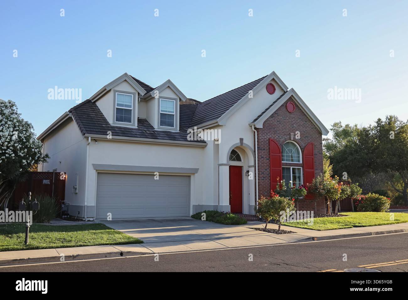 Une maison moderne de banlieue avec une porte et des volets rouges, avec un garage pour deux voitures et un aménagement paysager bien entretenu Banque D'Images