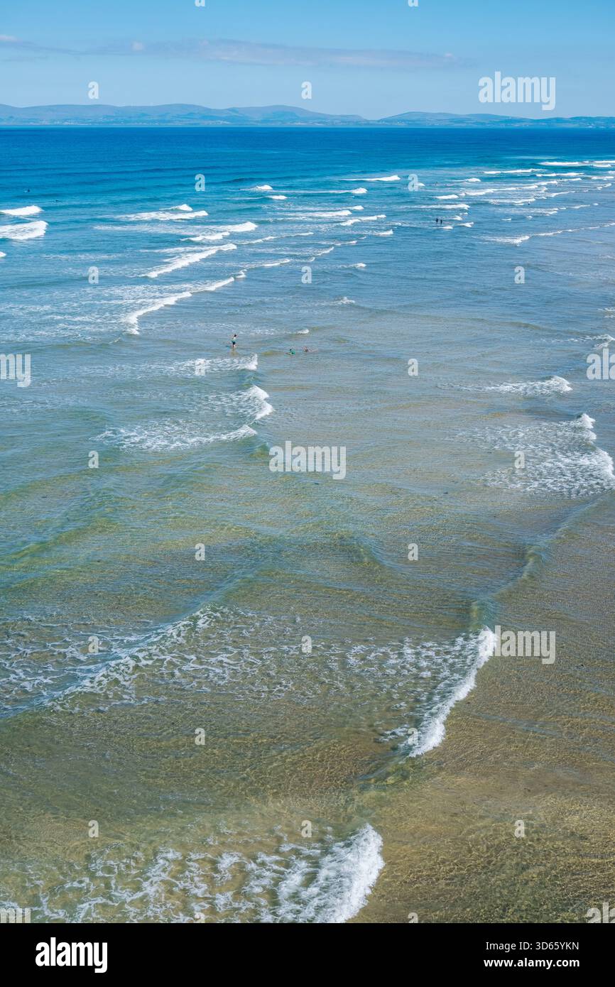 Les vagues tapent doucement contre le littoral sablonneux de Finner Beach, mettant en valeur les eaux turquoises claires sous un ciel bleu vif. Une atmosphère paisible inv Banque D'Images
