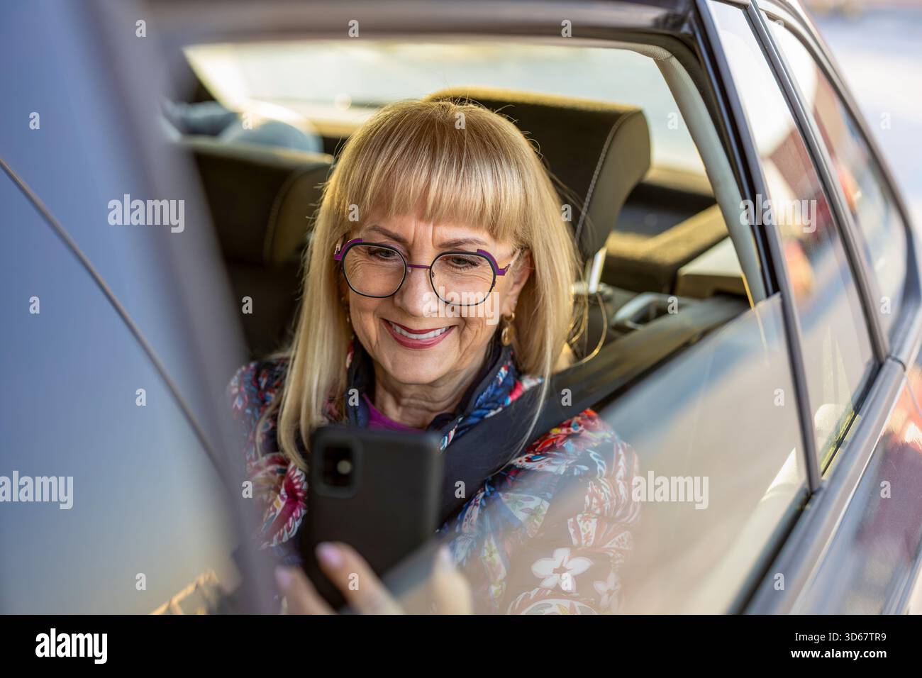 Femme senior assise sur le siège arrière à l'aide d'un smartphone Banque D'Images