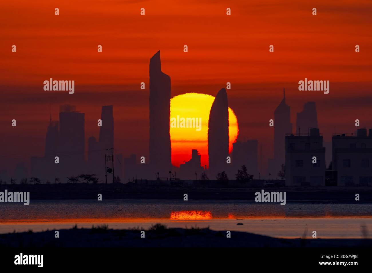 Le soleil se couche au-dessus d'une ville koweïtienne, projetant une lueur chaude sur les bâtiments. Le ciel est rempli de teintes orange et rose, créant une atmosphère sereine Banque D'Images