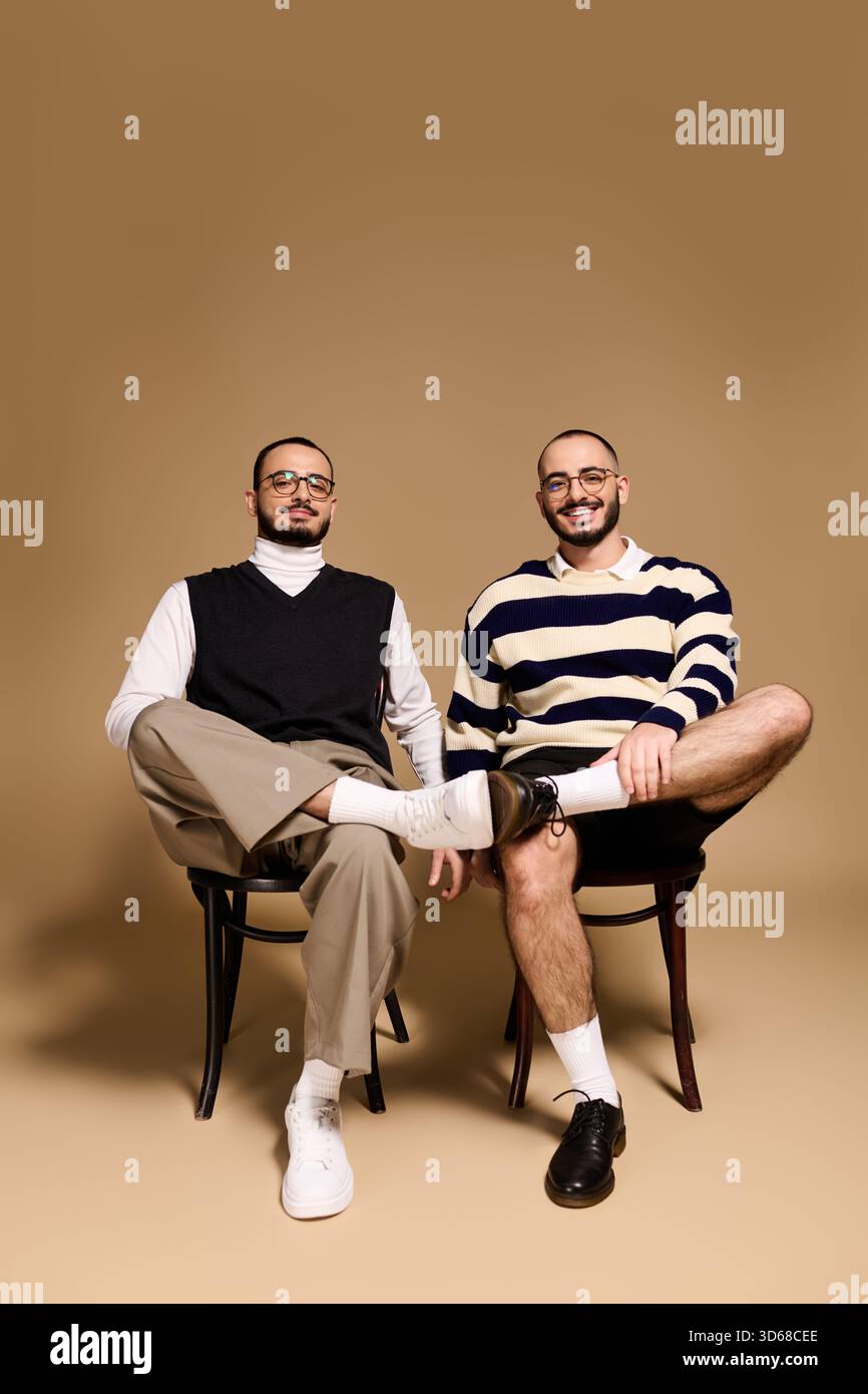 Deux frères jumeaux vêtus de tenues tendance posent en toute confiance dans un studio aux tons chauds. Banque D'Images