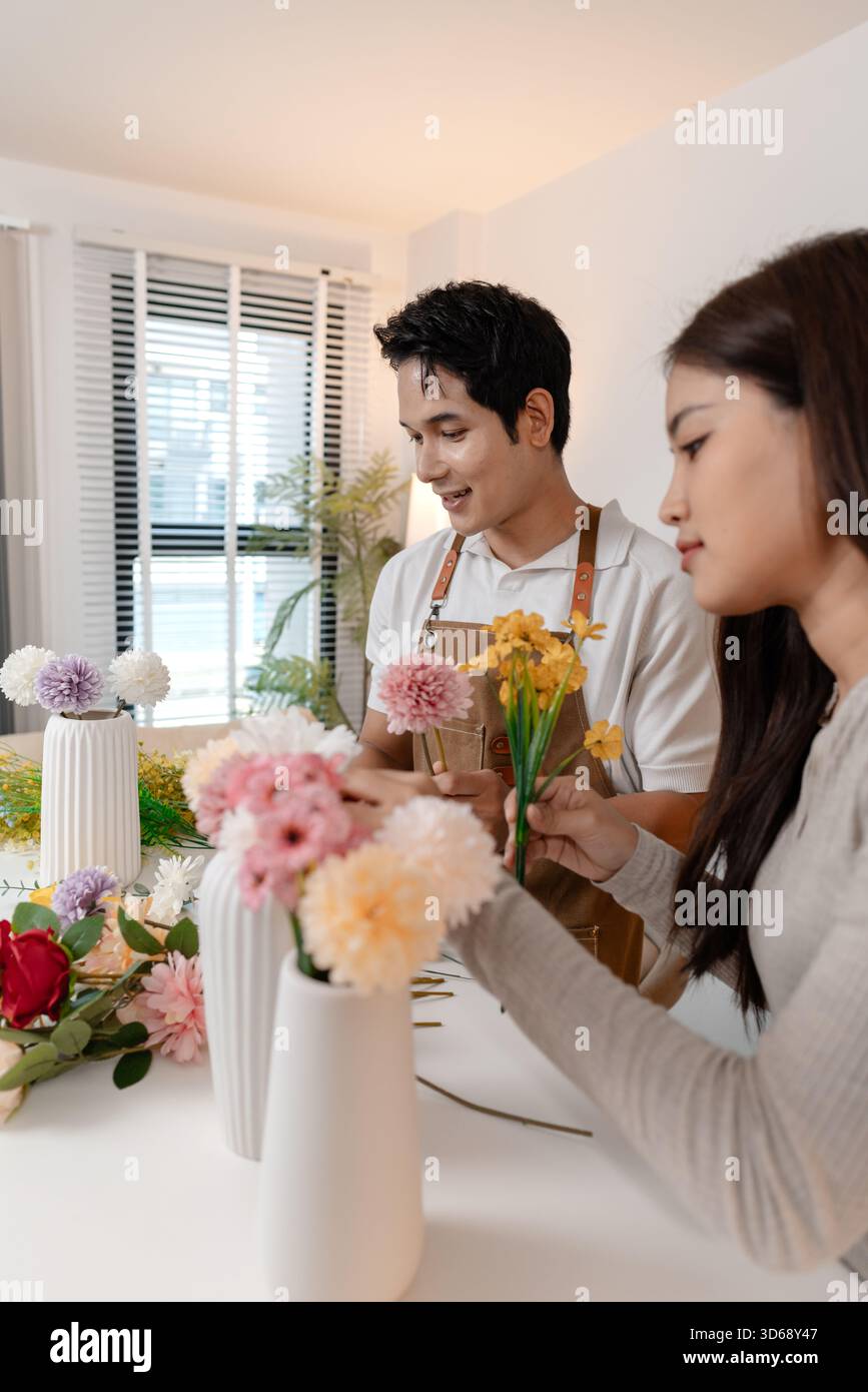 Un jeune couple arrangeant des fleurs colorées ensemble dans un cadre de maison confortable. L'homme, portant un tablier, aide la femme à créer un beau bouquet, shar Banque D'Images