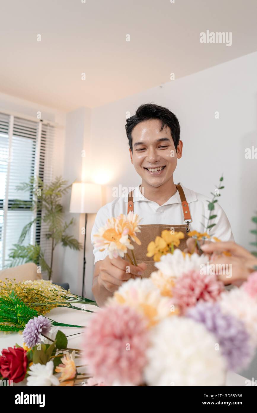 Un jeune couple arrangeant des fleurs colorées ensemble dans un cadre de maison confortable. L'homme, portant un tablier, aide la femme à créer un beau bouquet, shar Banque D'Images