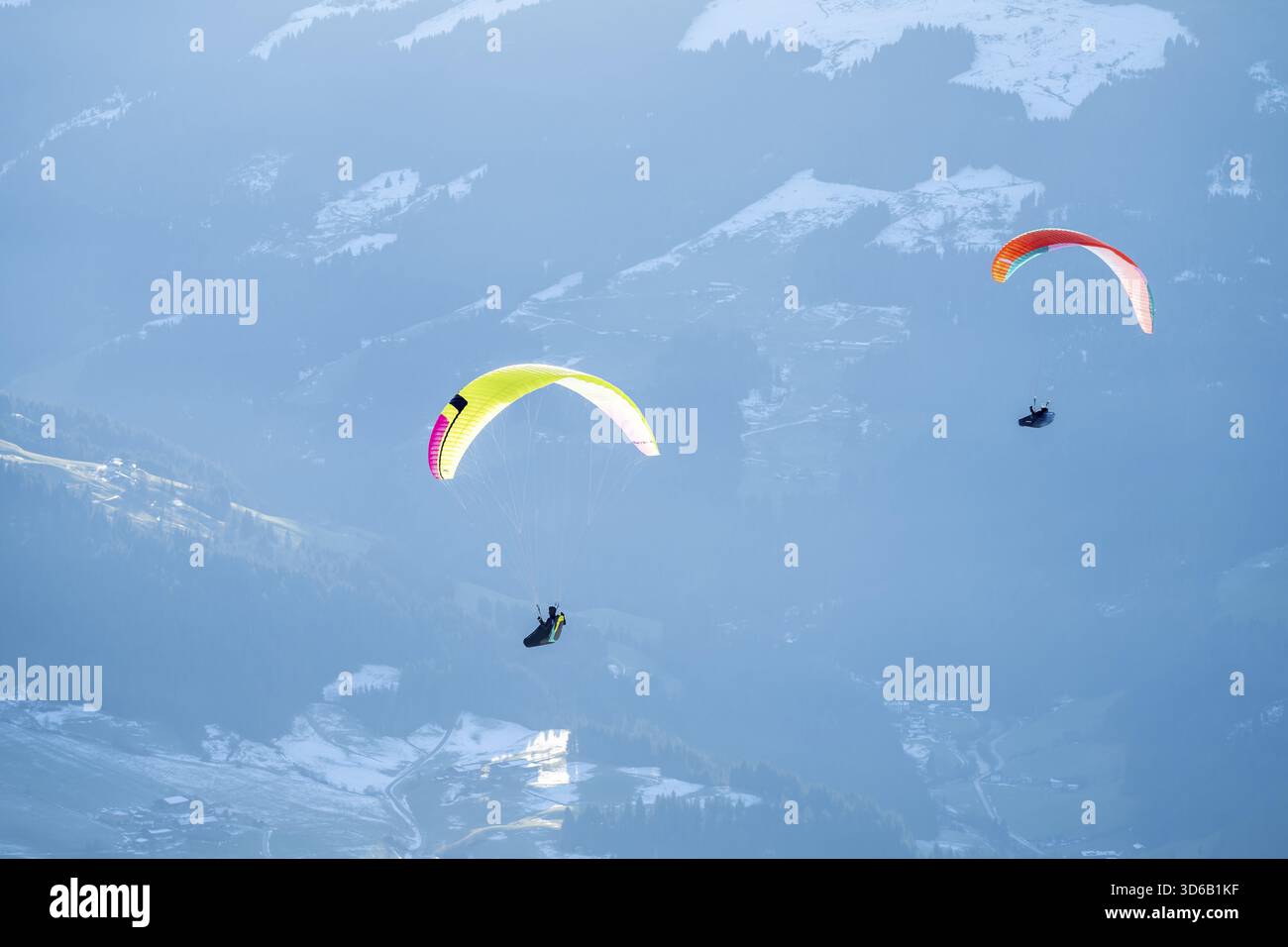 Deux parapentes volant devant des montagnes enneigées dans la lumière du soir en hiver, Alpes de Kitzbuehel, Tyrol, Autriche Banque D'Images