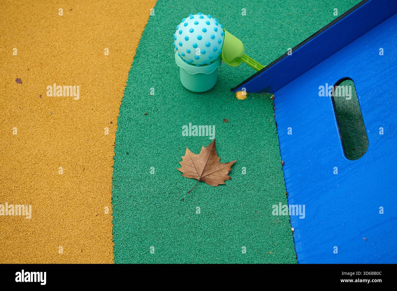 Terrain de jeu coloré avec gazon vert, sol jaune, toboggan bleu et un lea d'automne brun, un cadre extérieur ludique évoquant le plaisir en plein air et le cha saisonnier Banque D'Images