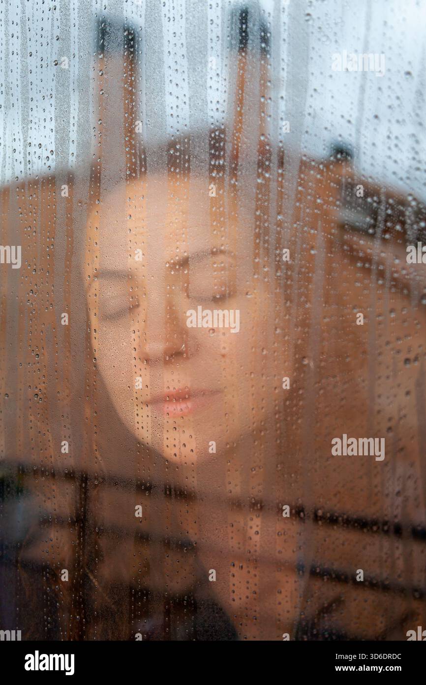 Portrait authentique d'une femme regardant la pluie derrière Wet Glass. Banque D'Images