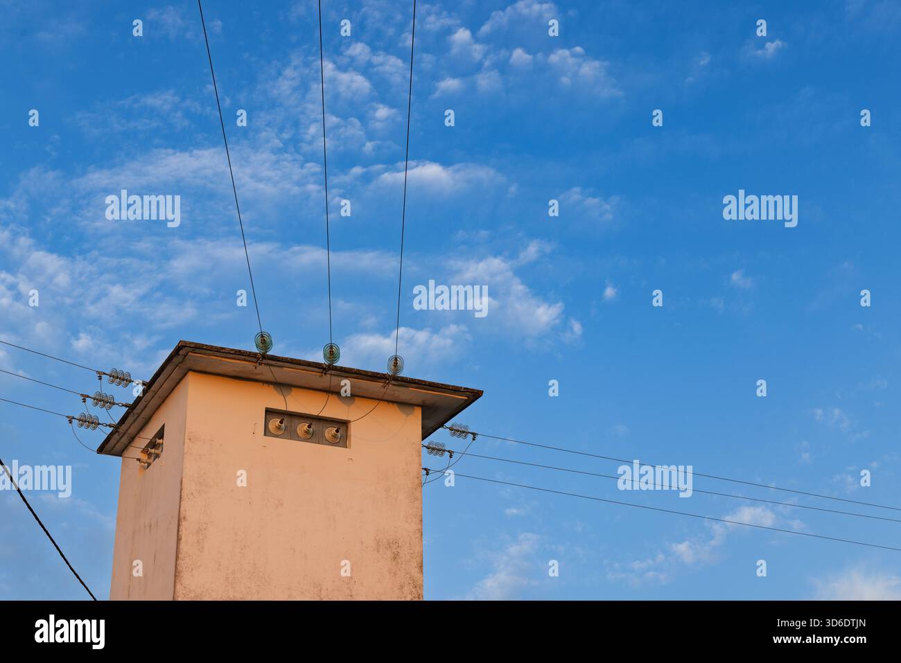 Un bâtiment de transformateur électrique en béton, ou sous-station de distribution, avec des lignes électriques et des isolants en verre contre un ciel bleu doux et nuageux au crépuscule. Banque D'Images