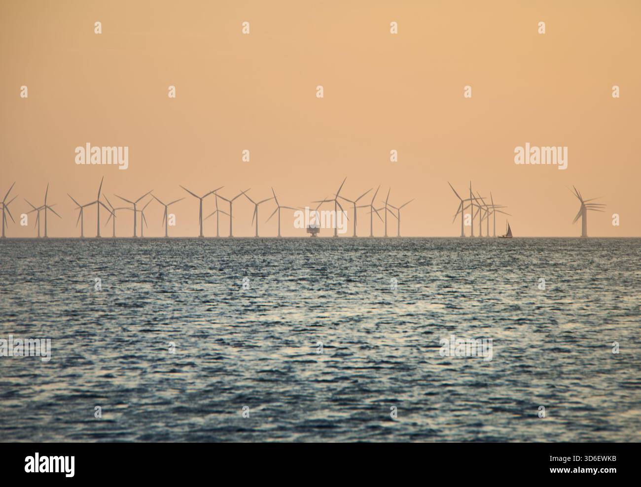Éoliennes offshore, parc éolien se tenant dans la mer au coucher du soleil, symbolisant l'énergie propre, la durabilité et les ressources renouvelables avec un océan tranquille Banque D'Images
