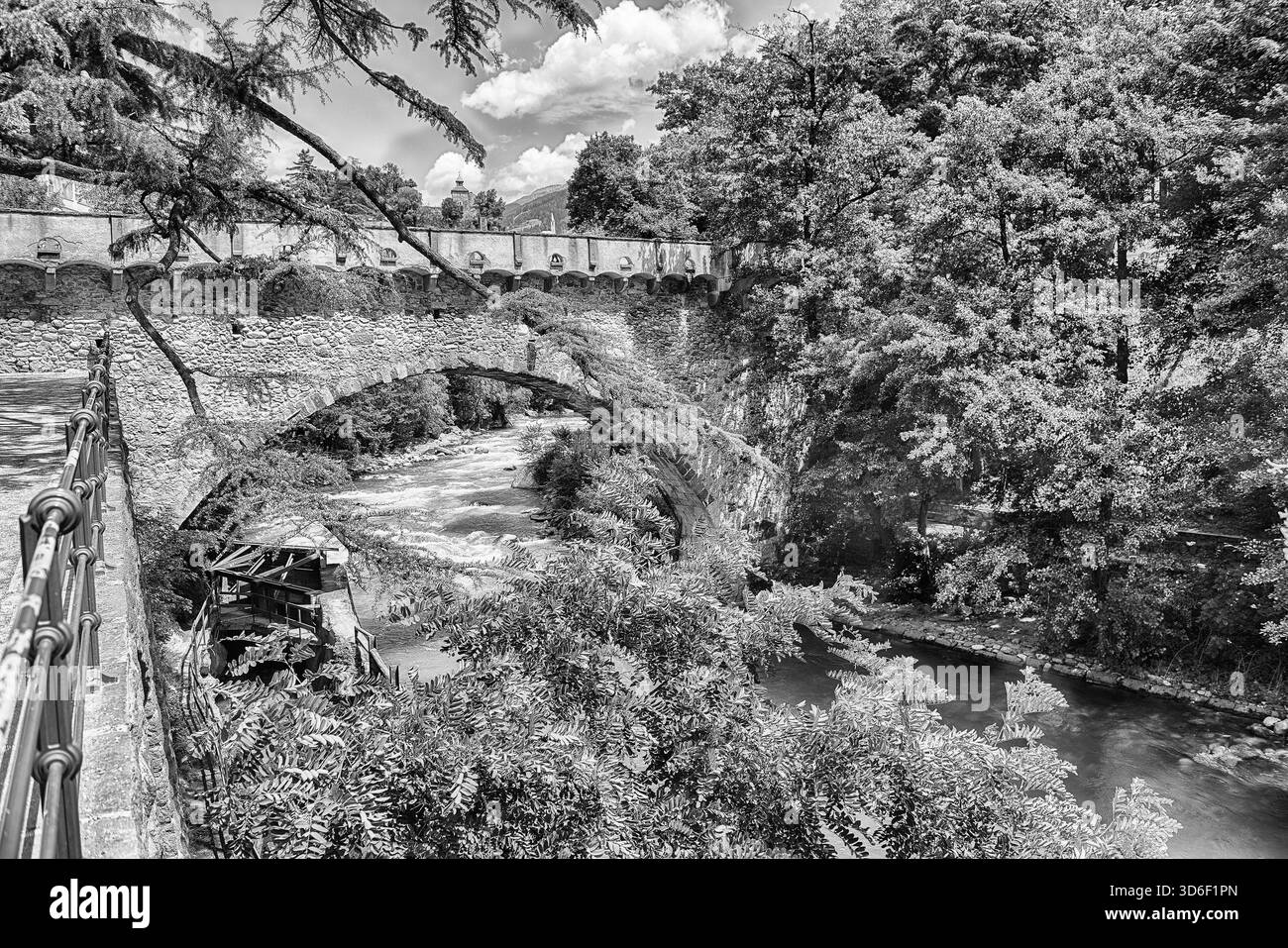 Vue du pont Steinerner Steg traversant une rivière avec des arbres verdoyants des deux côtés, monument emblématique de Merano, Tyrol du Sud, Italie Banque D'Images