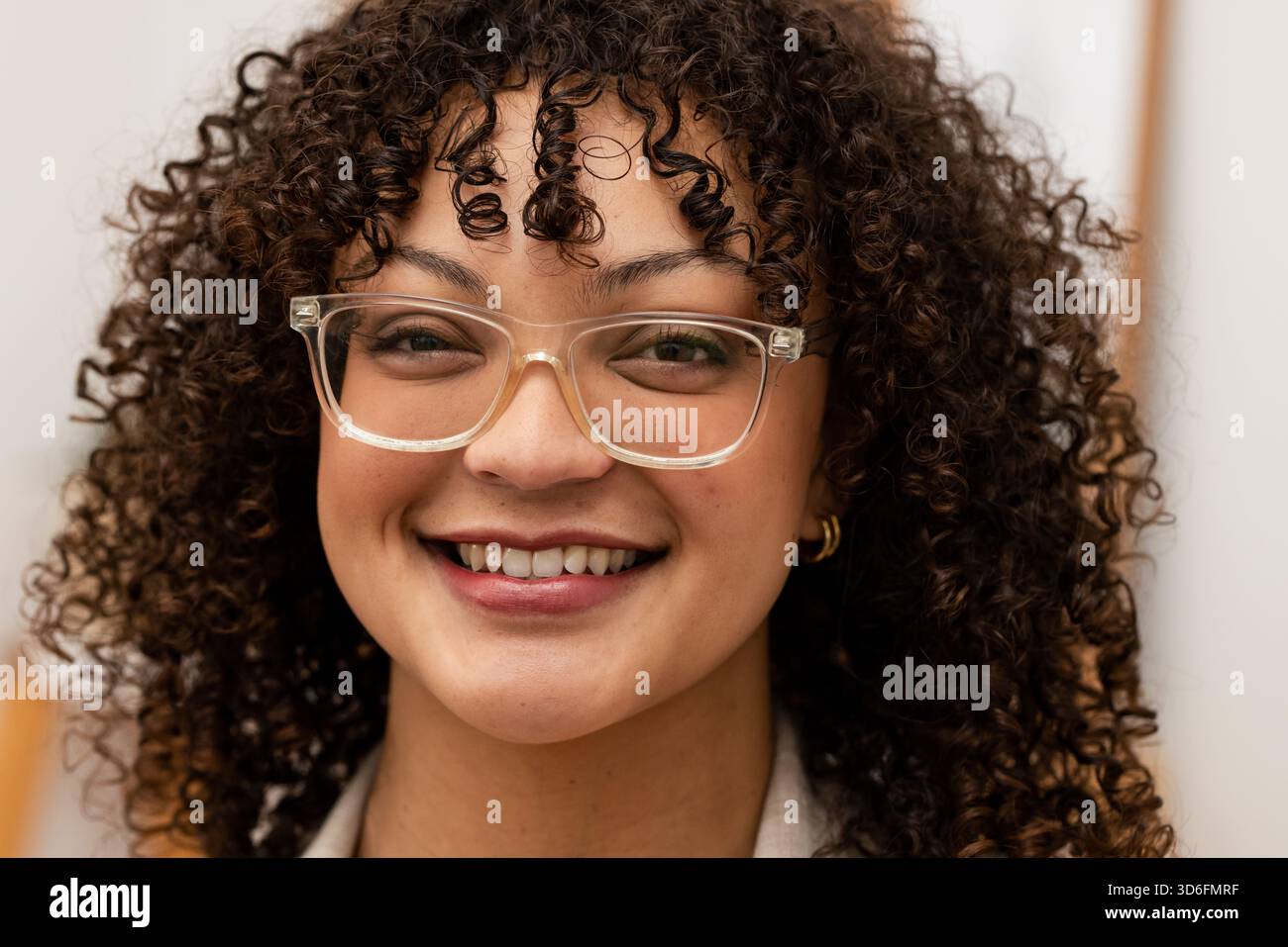 Femme souriant tout en portant des lunettes à cadre clair et de petites boucles d'oreilles en or dans le portrait de bureau Banque D'Images