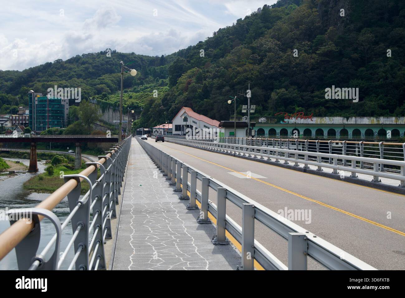 Une passerelle piétonne longe le pont Gangchon avec des garde-corps et des lampadaires, tandis que la vallée de la rivière, les toits du village et la longue arcade sur les oppos Banque D'Images