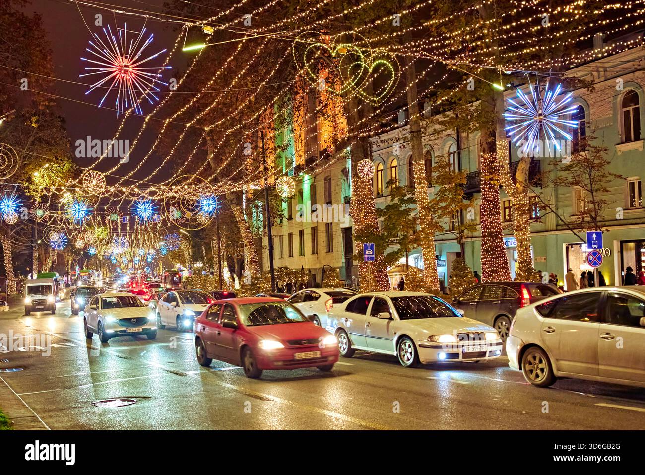 Embouteillage lourd sur une rue urbaine décorée de guirlandes suspendues brillantes et de lumières colorées pendant la nuit de la saison des vacances d'hiver. Banque D'Images