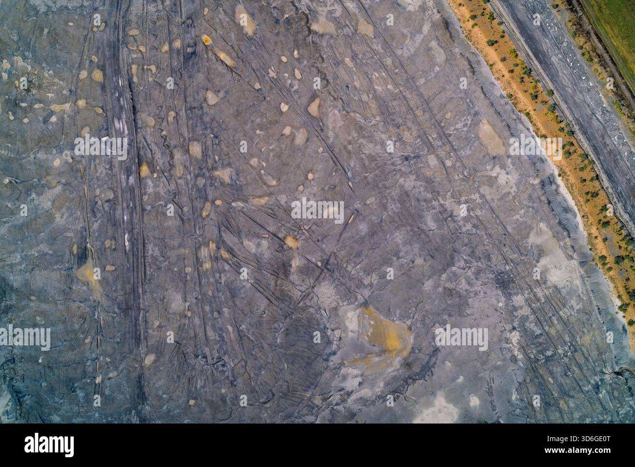 Vue aérienne de haut en bas d'une zone sèche et fissurée de déchets industriels (tas de déblais) montrant les traces de pneus, les taches d'eau et l'érosion. Schéma abstrait de la dégradation des terres et de la pollution. Banque D'Images