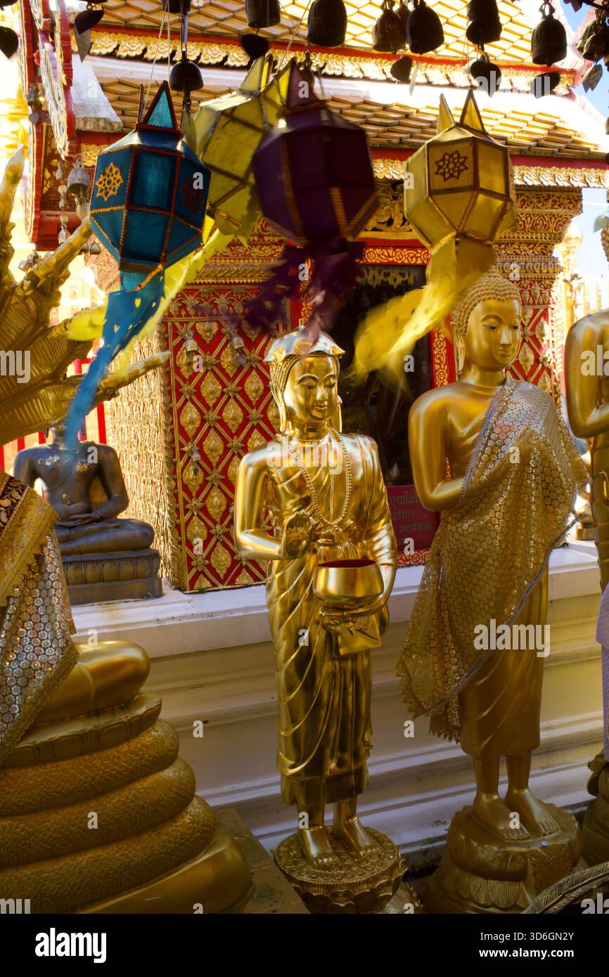 Statues debout et dorées de Bouddha dans diverses poses avec des lanternes bleues, violettes et jaunes remuant dans le vent avec des streamers flous et mobiles. Banque D'Images