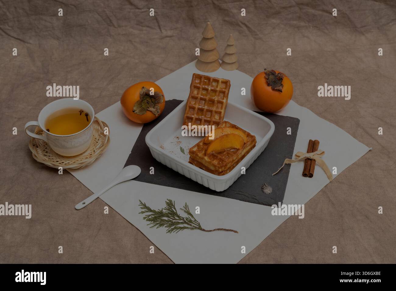 Nature morte rustique d'hiver avec gaufres belges, kakis et une tasse de tisane sur un fond de toile beige Banque D'Images