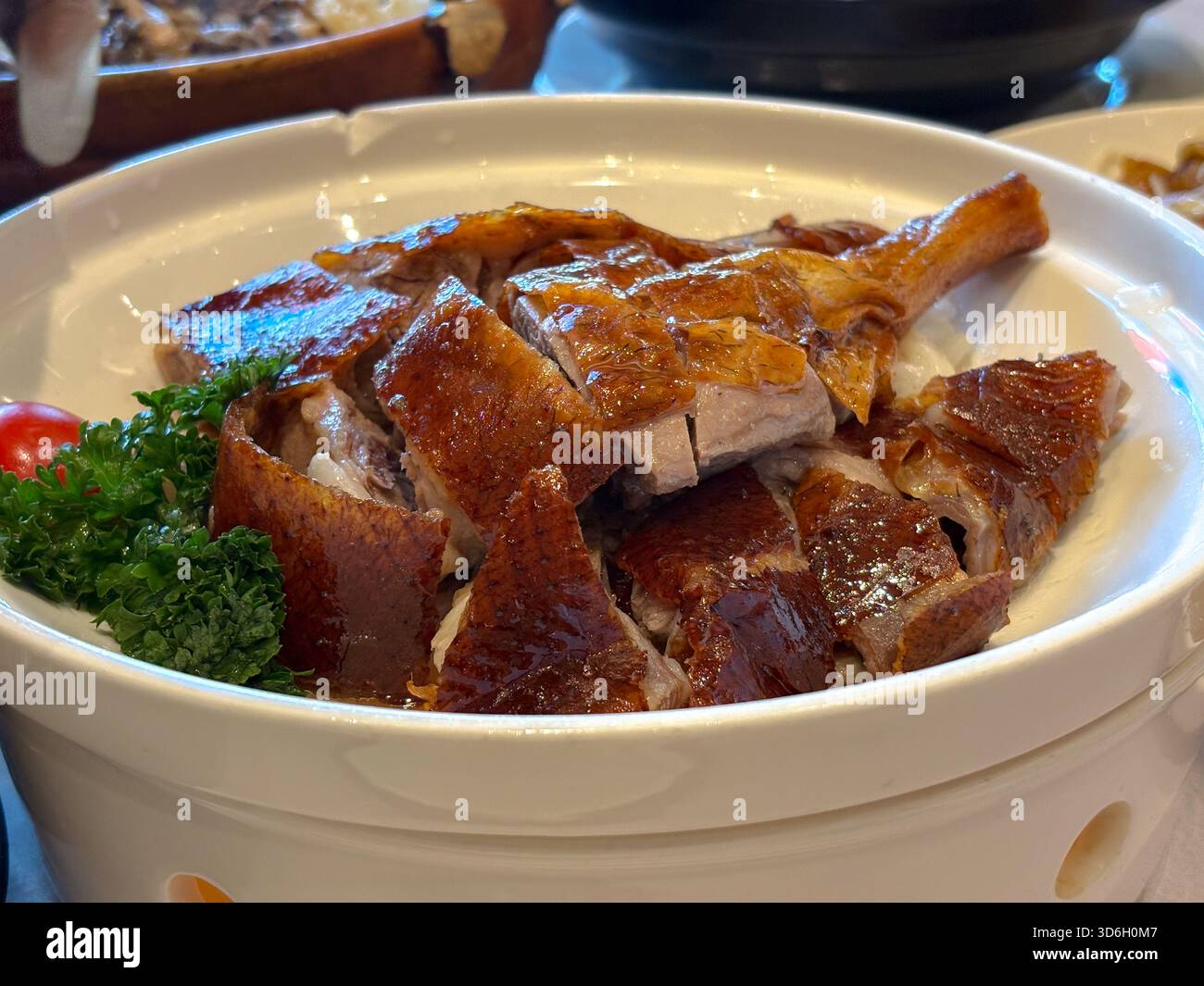 Oie rôtie à la peau croustillante dorée, tranchée et servie dans un plat en céramique blanche, garnie de légumes verts et de tomates. Cuisine chinoise traditionnelle de Kai Banque D'Images