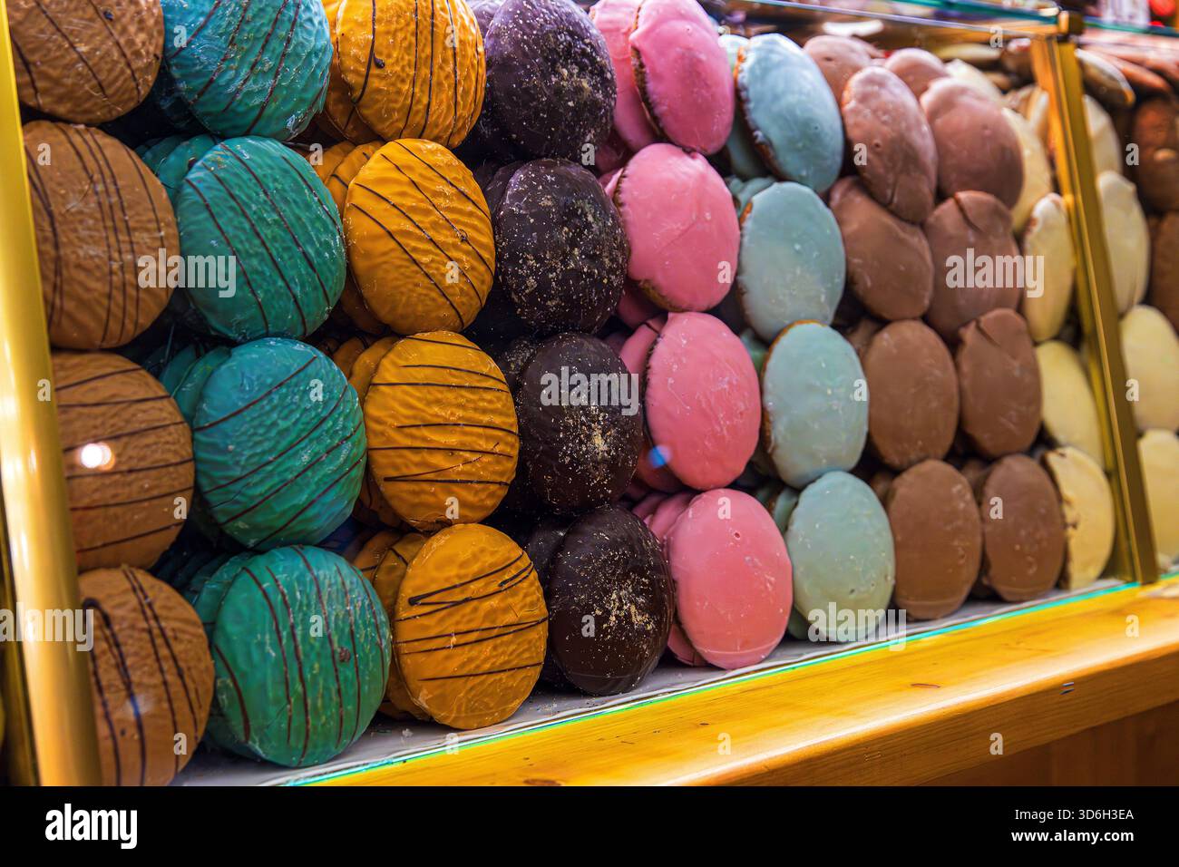 Assortiment de ronds de pain d'épices vibrants décorés à la main en plusieurs couleurs et textures, disposés derrière un comptoir en verre avec réflexion lumineuse festive Banque D'Images