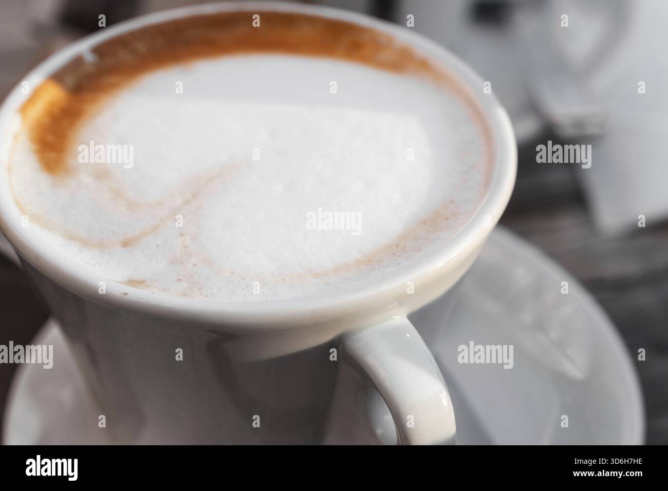 Gros plan d'un cappuccino fraîchement préparé avec de la mousse de lait servi dans une tasse en céramique blanche, avec un léger tourbillon de café le long du bord Banque D'Images