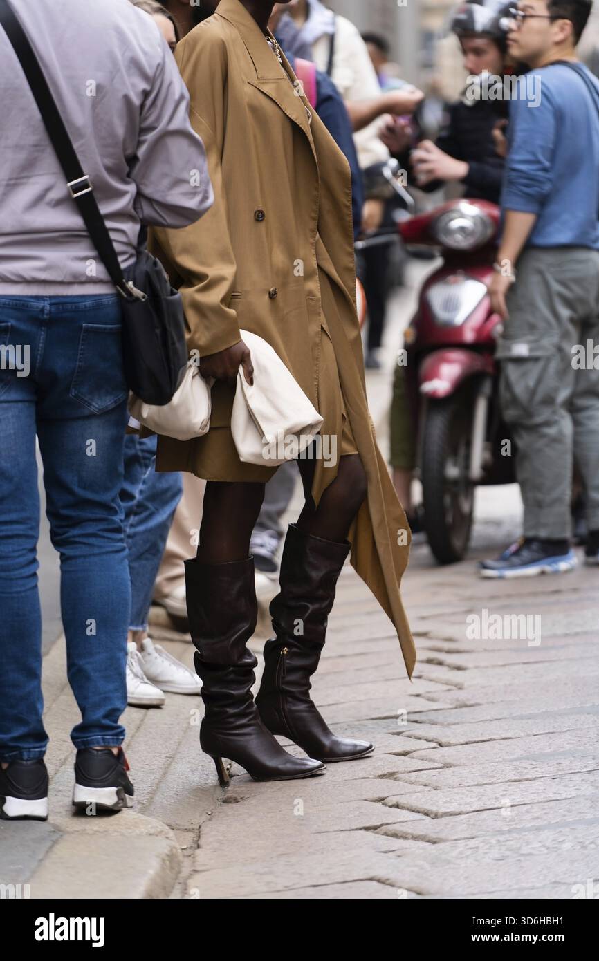Milan, Italie - septembre, 21, 2022: Les femmes élégantes portant un manteau brun chameau, jupe assortie et brassière, marron talons hauts bottes en cuir, tenant beige Banque D'Images