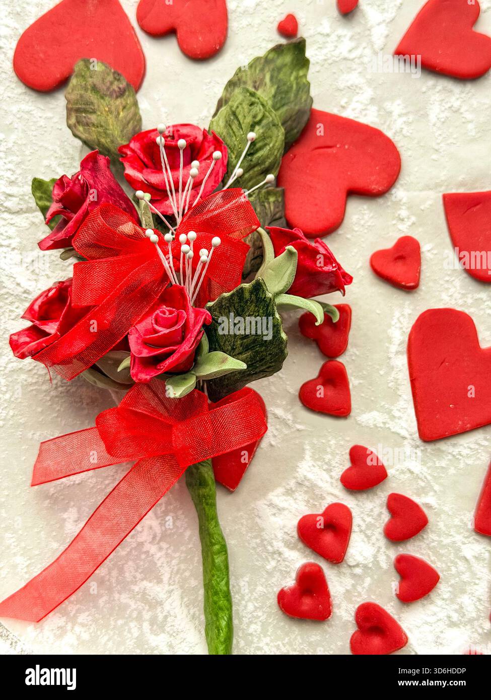 Bouquet artificiel de roses rouges avec ruban entouré de formes de coeur de sucre glace rouge dispersées sur fond clair texturé, sugarcraft Banque D'Images