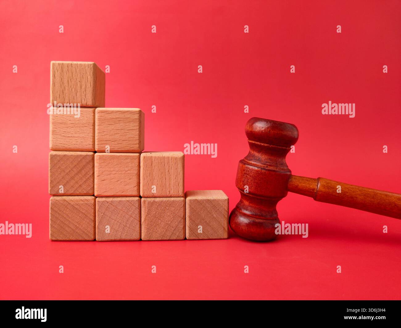L'image montre un marteau en bois à côté d'une pile de cubes en bois sur un fond rouge. Banque D'Images