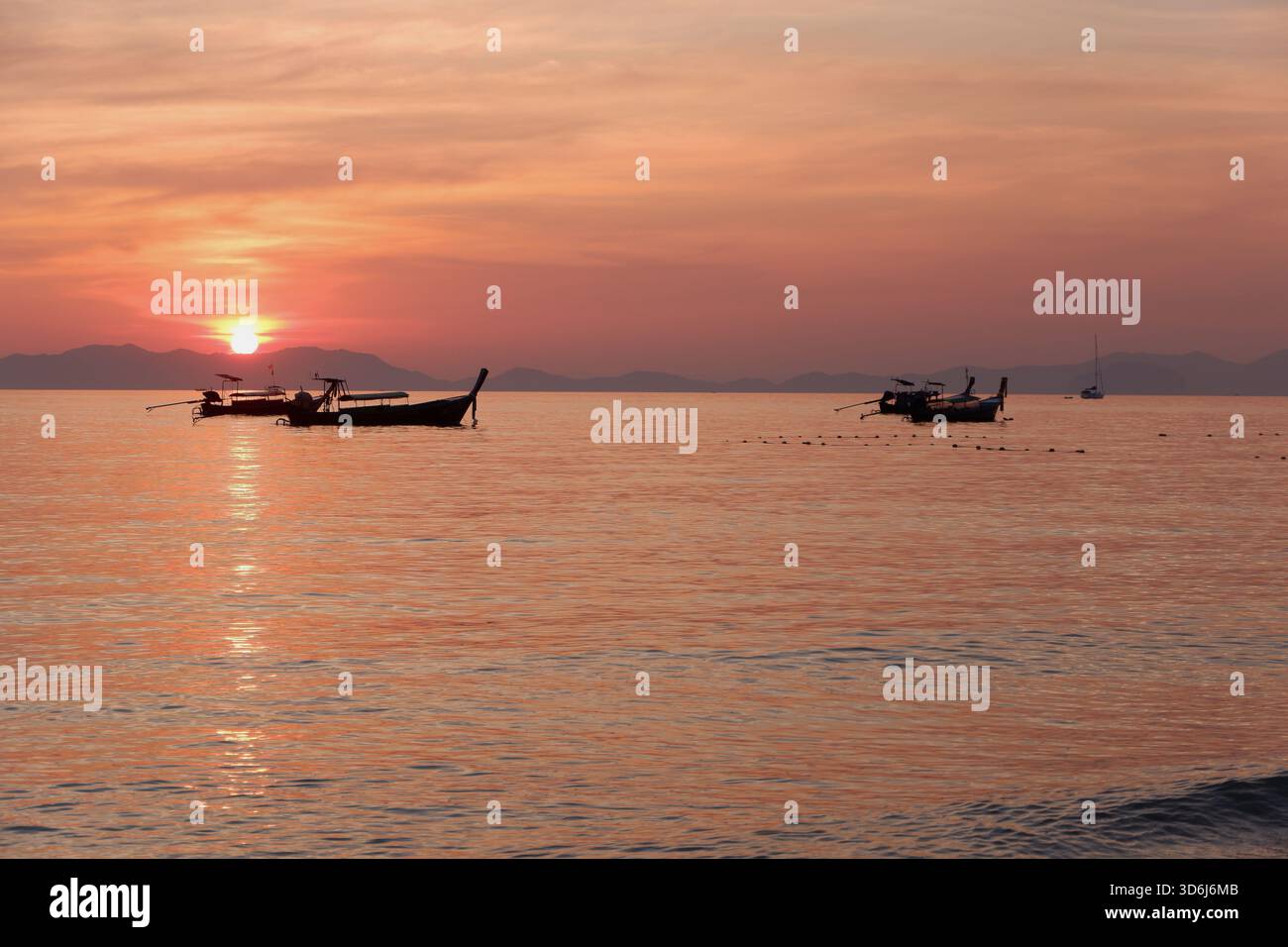 Les bateaux à longue queue dérivent tranquillement à travers de douces vagues sous un coucher de soleil chaud, reflétant une douce lumière dorée sur l'eau tranquille. Banque D'Images
