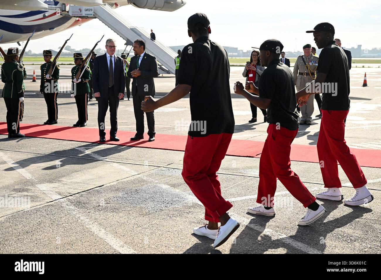 Le premier ministre Sir Keir Starmer (à gauche) regarde le groupe de danse Fire and Ivory Pantsula se produire alors qu’il est accueilli par un responsable sud-africain à son arrivée à l’aéroport international O.R. Tambo avant le sommet du G20 à Johannesburg, en Afrique du Sud. Date de la photo : vendredi 21 novembre 2025. Banque D'Images