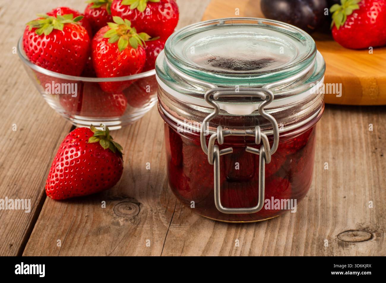 Pot en verre de confiture de fraises placé sur une table en bois avec des fraises fraîches en arrière-plan, créant un fruit naturel et concept alimentaire maison ide Banque D'Images