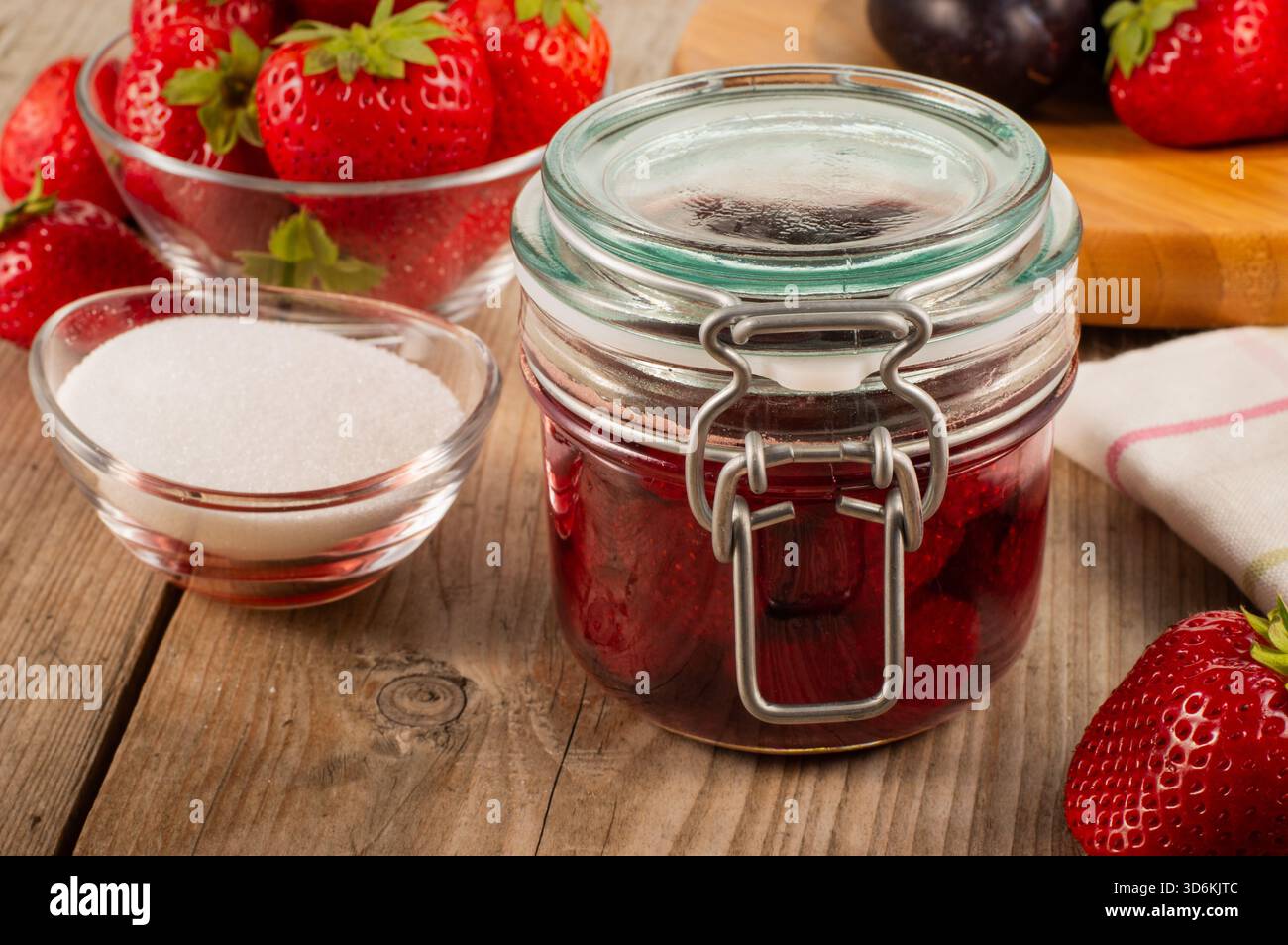 Pot de confiture de fraises sur une table en bois avec des fraises fraîches et un bol de sucre en arrière-plan, créant une nourriture maison rustique et une conce de fruits Banque D'Images