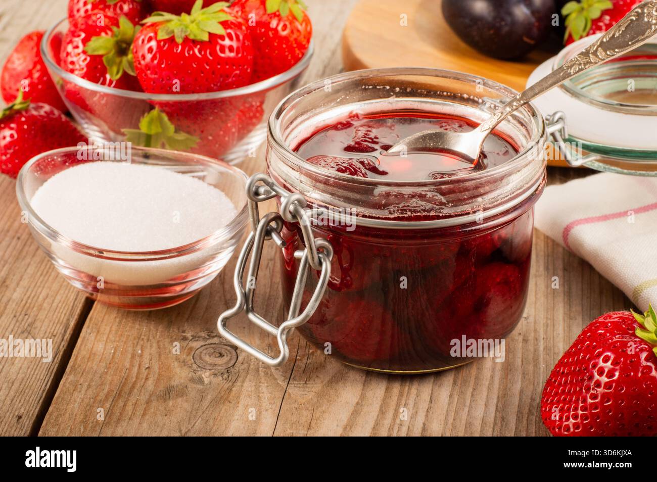 Pot de confiture de fraises sur une table en bois avec des fraises fraîches et un bol de sucre en arrière-plan, créant une nourriture maison rustique et une conce de fruits Banque D'Images