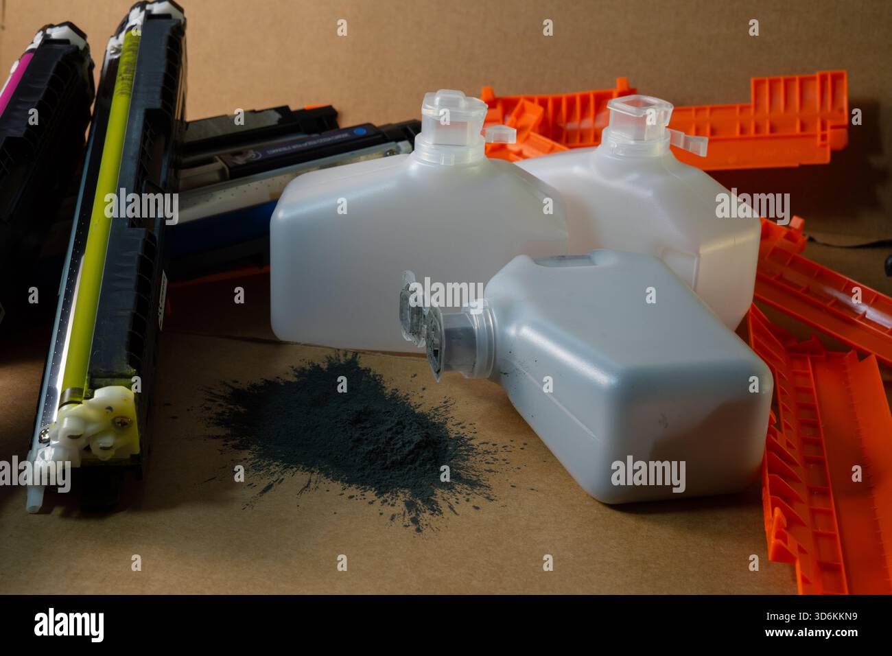 Cartouches d'imprimante colorées et bouteilles de toner gaspillées dispersées sur une surface en carton avec de la poudre noire renversée. Banque D'Images