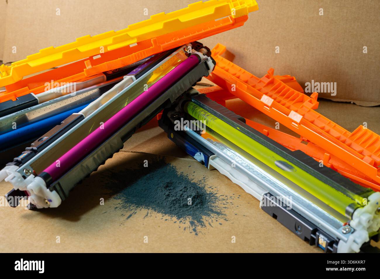 Gros plan de cartouches d'imprimante colorées avec de la poudre de toner noir renversée sur un fond en carton. Banque D'Images