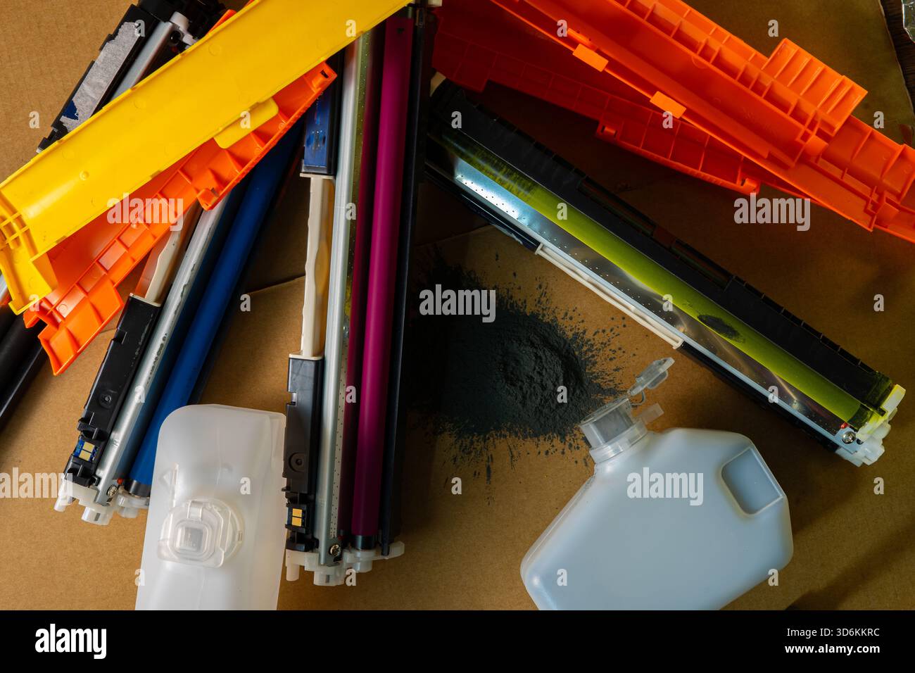 Cartouches d'imprimante colorées et bouteilles de toner gaspillées dispersées sur une surface en carton avec de la poudre noire renversée. Banque D'Images