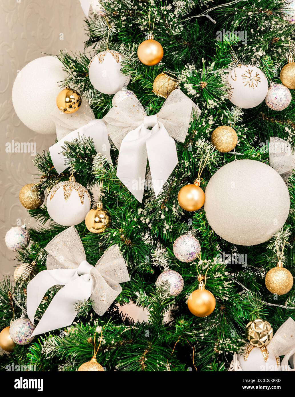 Gros plan d'un sapin de Noël magnifiquement décoré avec des ornements blancs et dorés, des noeuds étincelants et de la verdure givrée, créant un élégant et f Banque D'Images