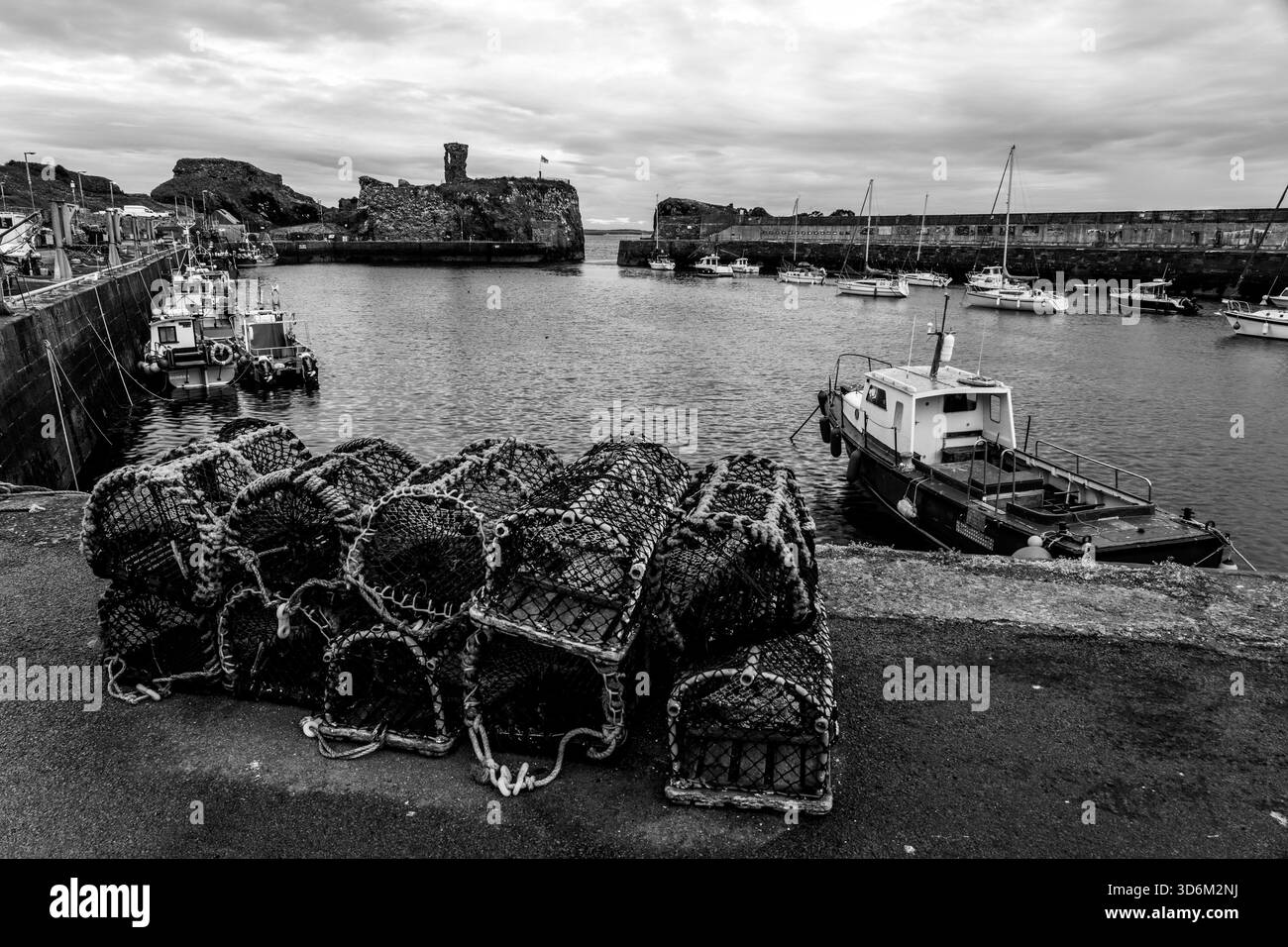 Casiers à homard et bateaux de pêche au port de Dunbar avec le château de Dunbar en ruine derrière en noir et blanc Banque D'Images