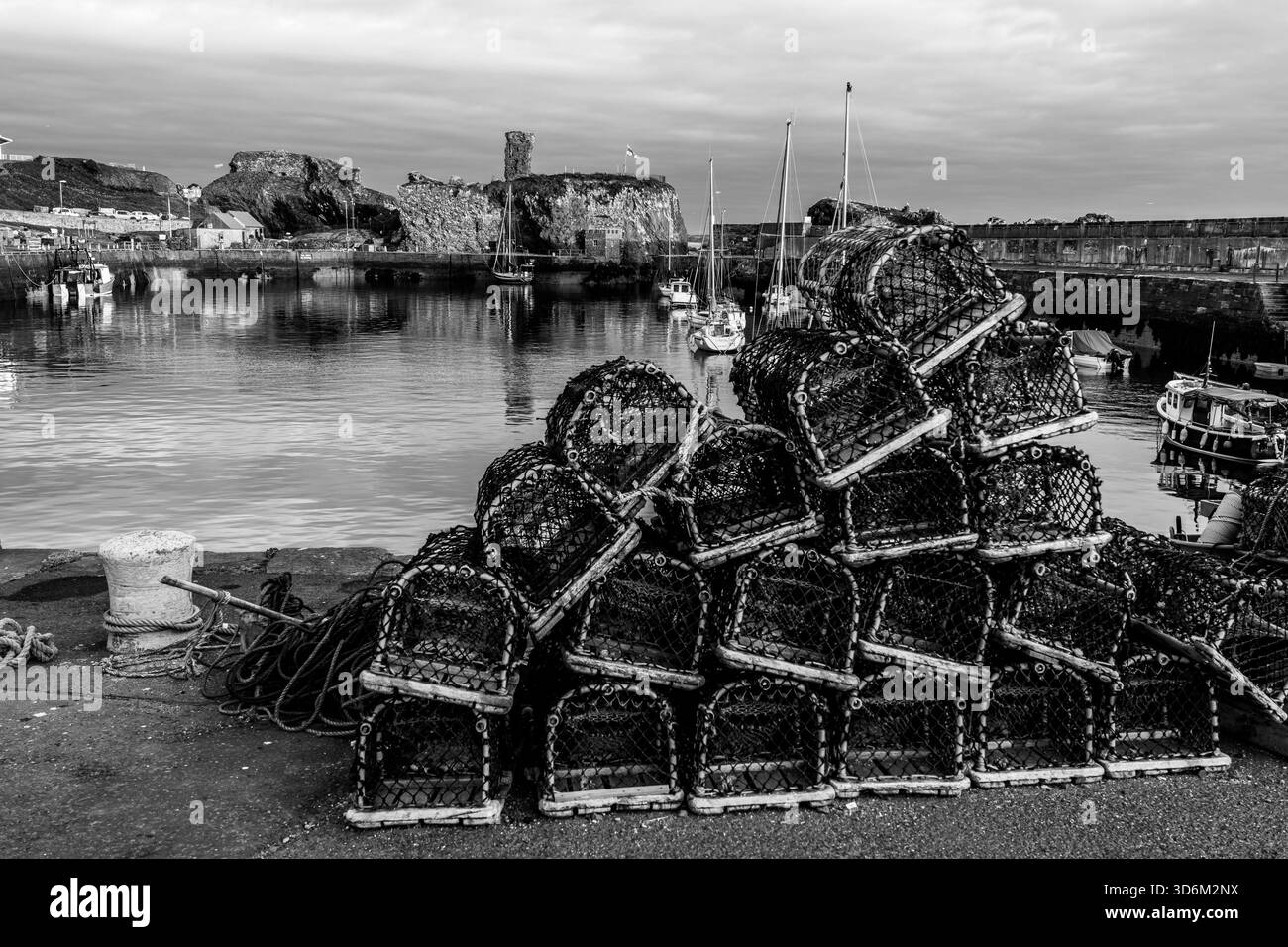 Vue en noir et blanc sur les casiers de homard au port de Dunbar avec le château de Dunbar derrière Banque D'Images