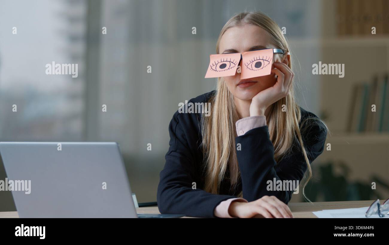 Humoristique femme d'affaires caucasienne avec des notes collantes sur les yeux lunettes à table avec faux ordinateur portable travaillant dans le bureau femme d'affaires fille féminine drôle Banque D'Images