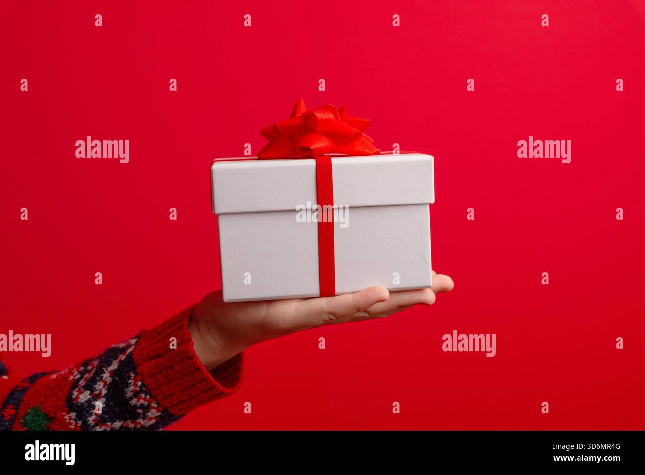 Boîte-cadeau reposant sur la main d'un enfant sur un fond rouge propre, idéale pour les publicités, les mises en page d'espace de copie, les ventes de vacances et les graphiques promotionnels Banque D'Images