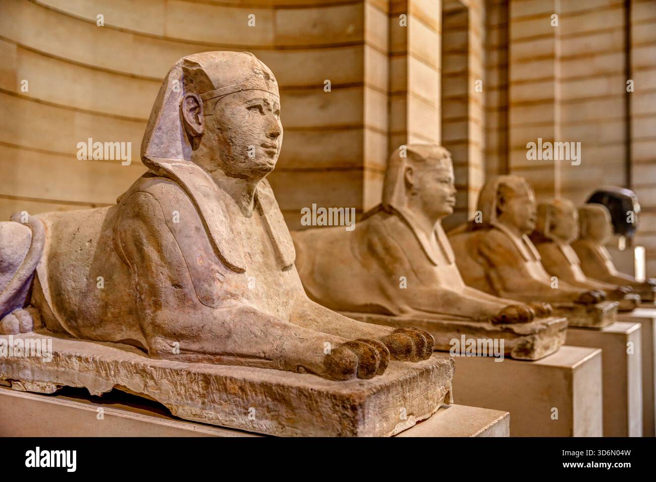 Rangée de statues de sphinx égyptiens anciennes exposées à l'intérieur du musée du Louvre à Paris, montrées dans une lumière chaude le long de la galerie bordée de pierres. Banque D'Images