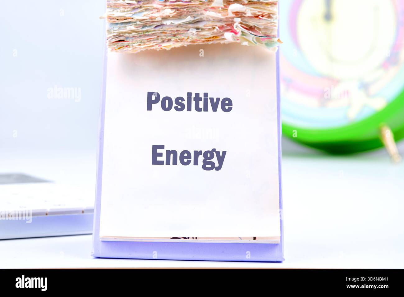 Un calendrier de bureau affiche les mots énergie positive. Il y a une horloge en arrière-plan et un clavier est à côté du calendrier, suggérant un productif Banque D'Images