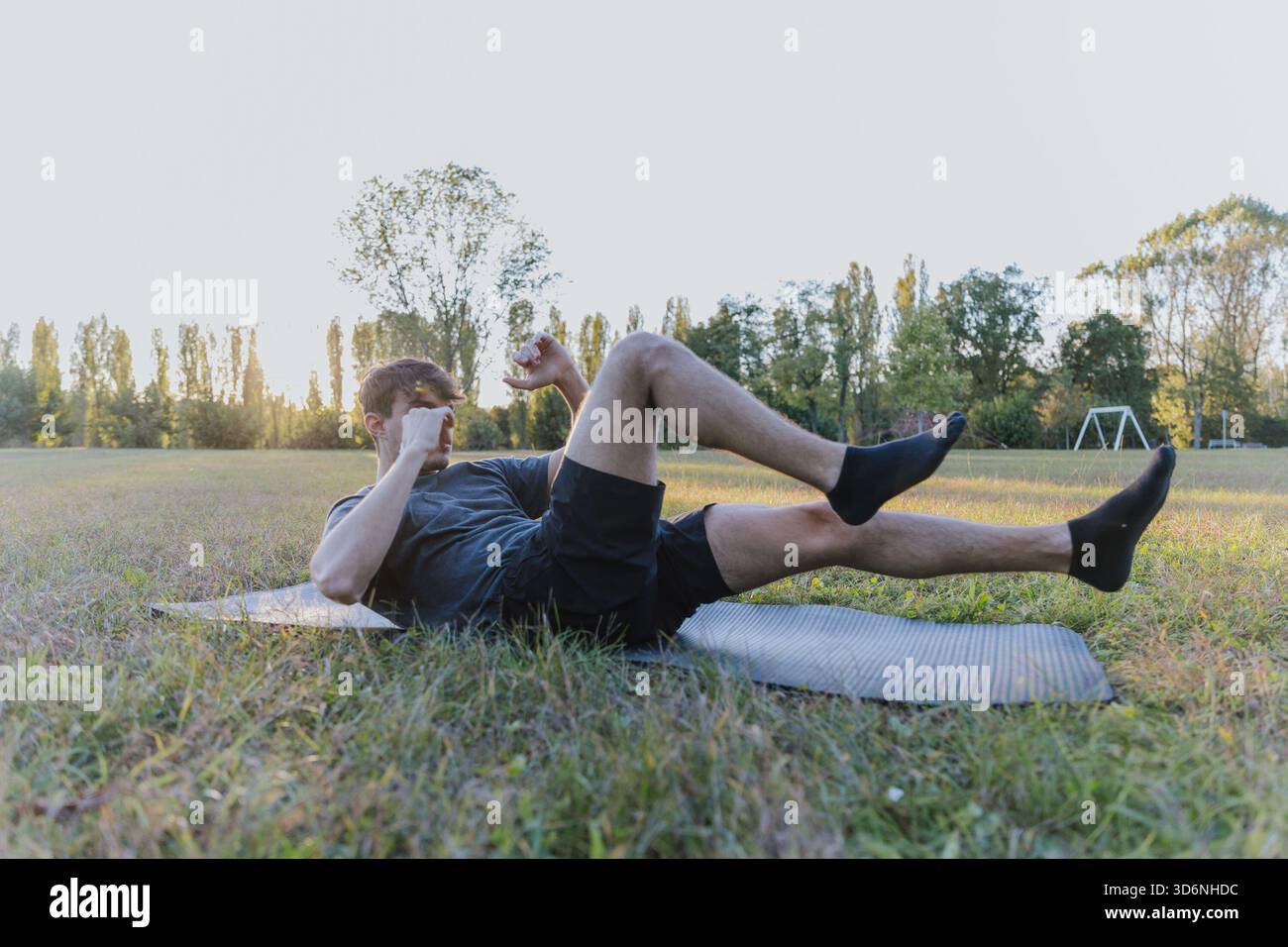 Un homme fait un exercice de cross-crawl sur un tapis dans un champ herbeux. La scène est paisible et sereine Banque D'Images