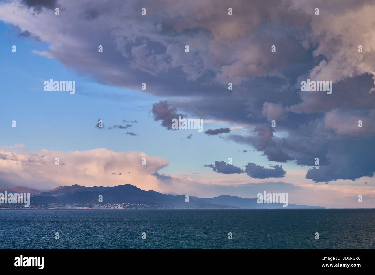 Nuages de tempête spectaculaires au-dessus de la mer calme au coucher du soleil derrière Mountain Horizon Banque D'Images