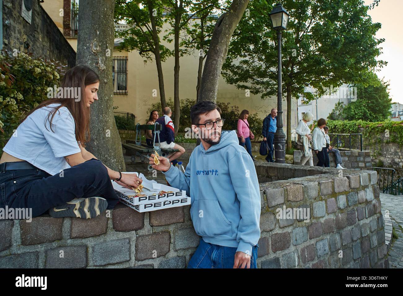 Paris, France - mars 2025 : couples et amis se réunissent au Square Roland Dorgelès à Montmartre. Un jeune homme et une jeune femme partagent une pizza tout en se prélassant dans le Banque D'Images