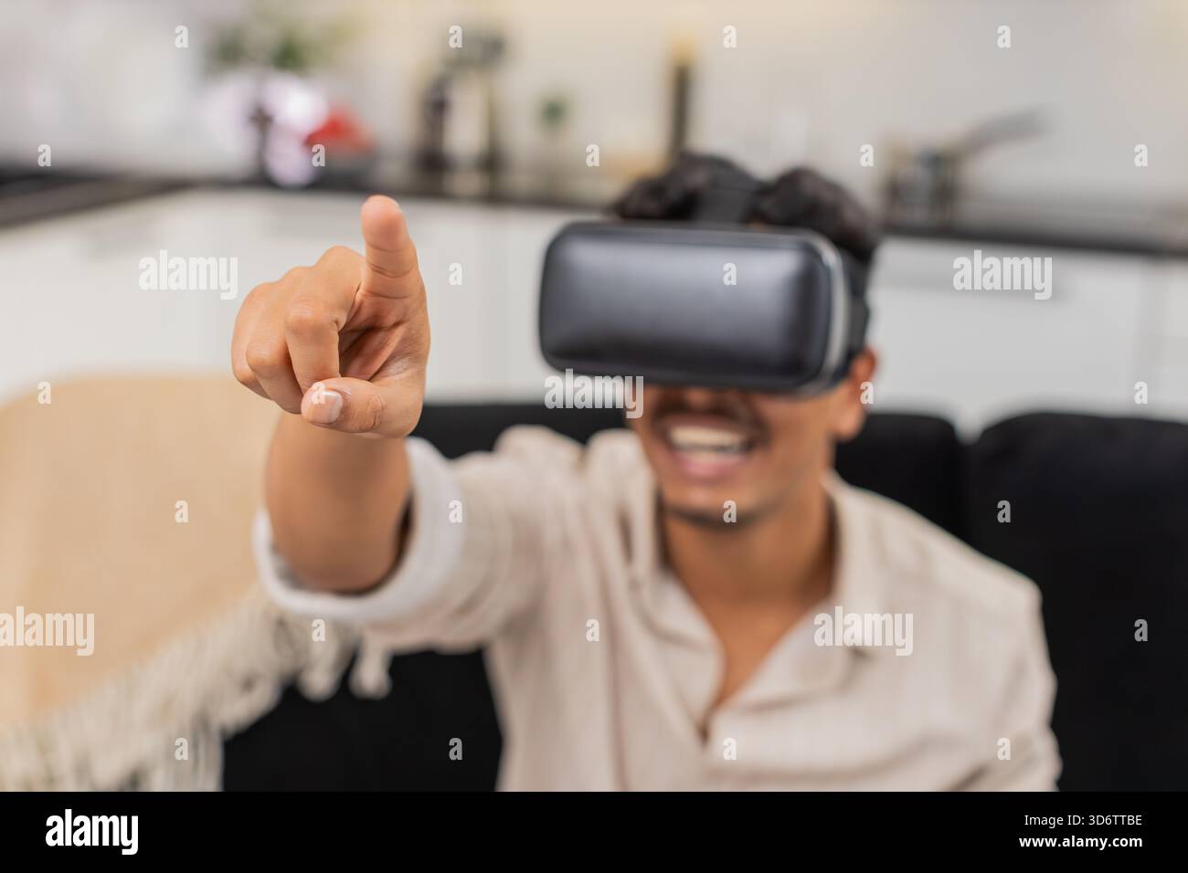 L'homme indien à la maison utilise le casque VR déplace les mains joue un jeu interactif et sourit avec surprise. Arabian Guy on sofa Watches contenu en ligne dit wow réagit avec des mots courts et hoche la tête dans le sourire de joie Banque D'Images