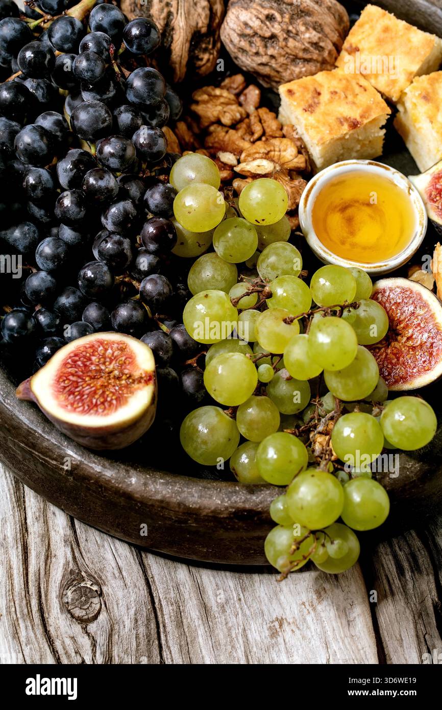 Hors-d'œuvre au vin avec différents raisins, figues, noix, pain, miel et fromage de chèvre sur plaque de céramique sur fond de bois ancien. Gros plan Banque D'Images