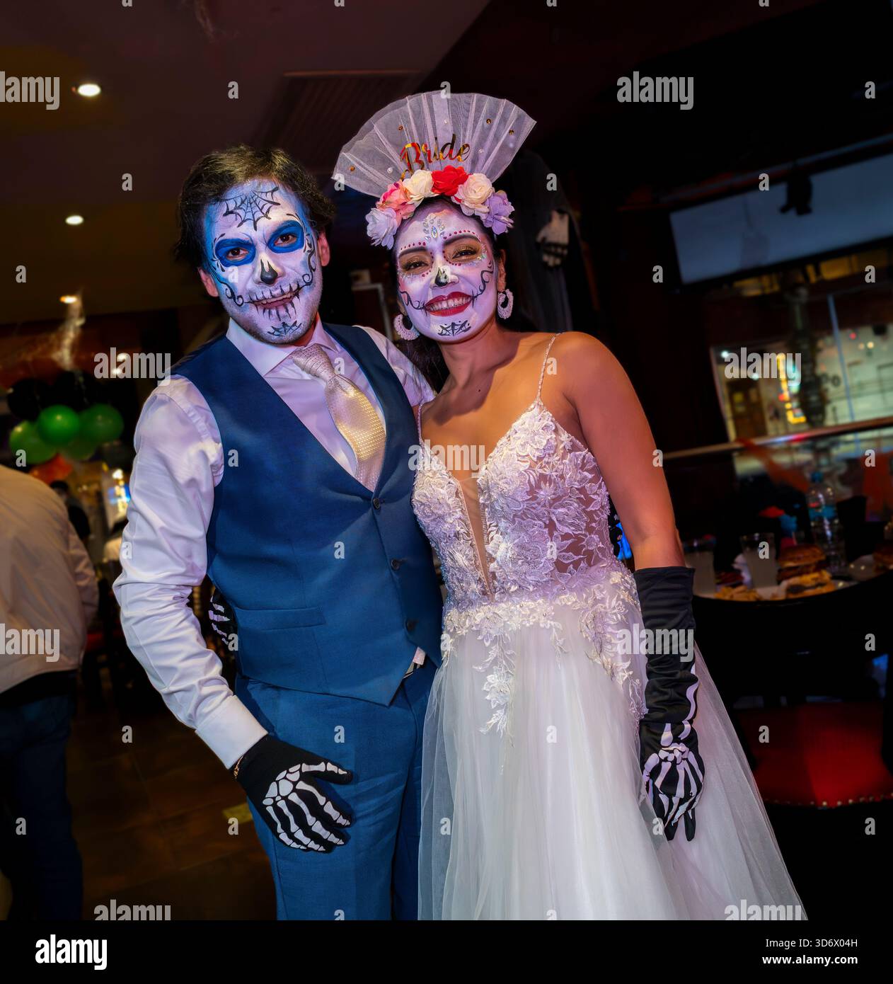 Couple dans le thème du maquillage d'Halloween et des costumes de style mariage posant lors d'un événement festif en intérieur avec des décorations colorées et de la peinture artistique pour le visage. Banque D'Images
