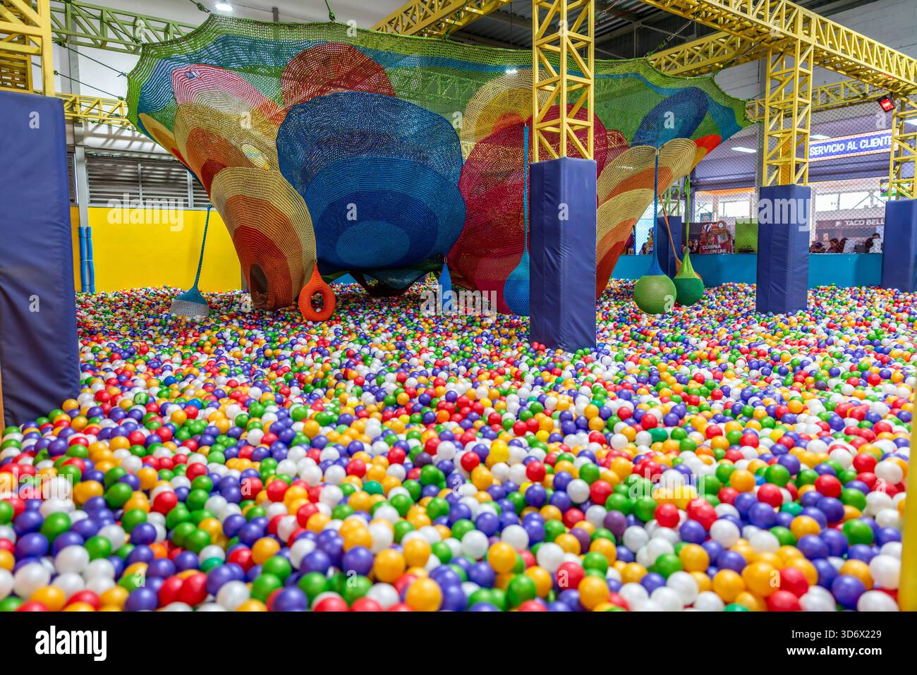 Fosse de balle pour enfants intérieure documentaire avec structure de jeu en filet suspendue colorée, poteaux souples et zone de loisirs vibrante remplie de balles multicolores. Banque D'Images