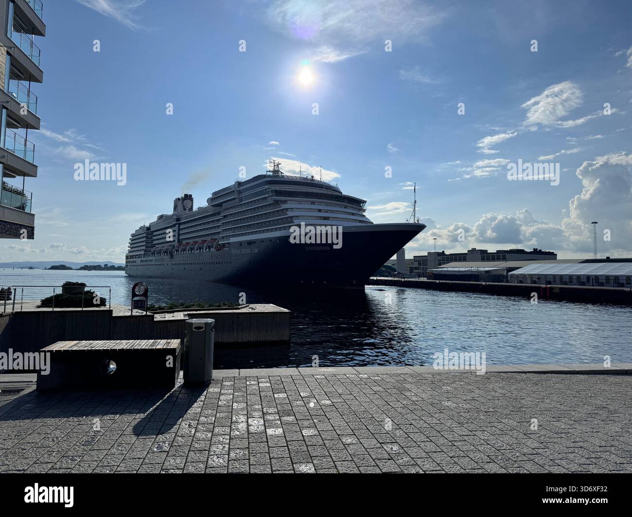 Un énorme bateau de croisière pénètre dans le port, la lumière du soleil se reflétant sur l'eau et la passerelle de la ville. - Image de stock capturée avec un smartphone