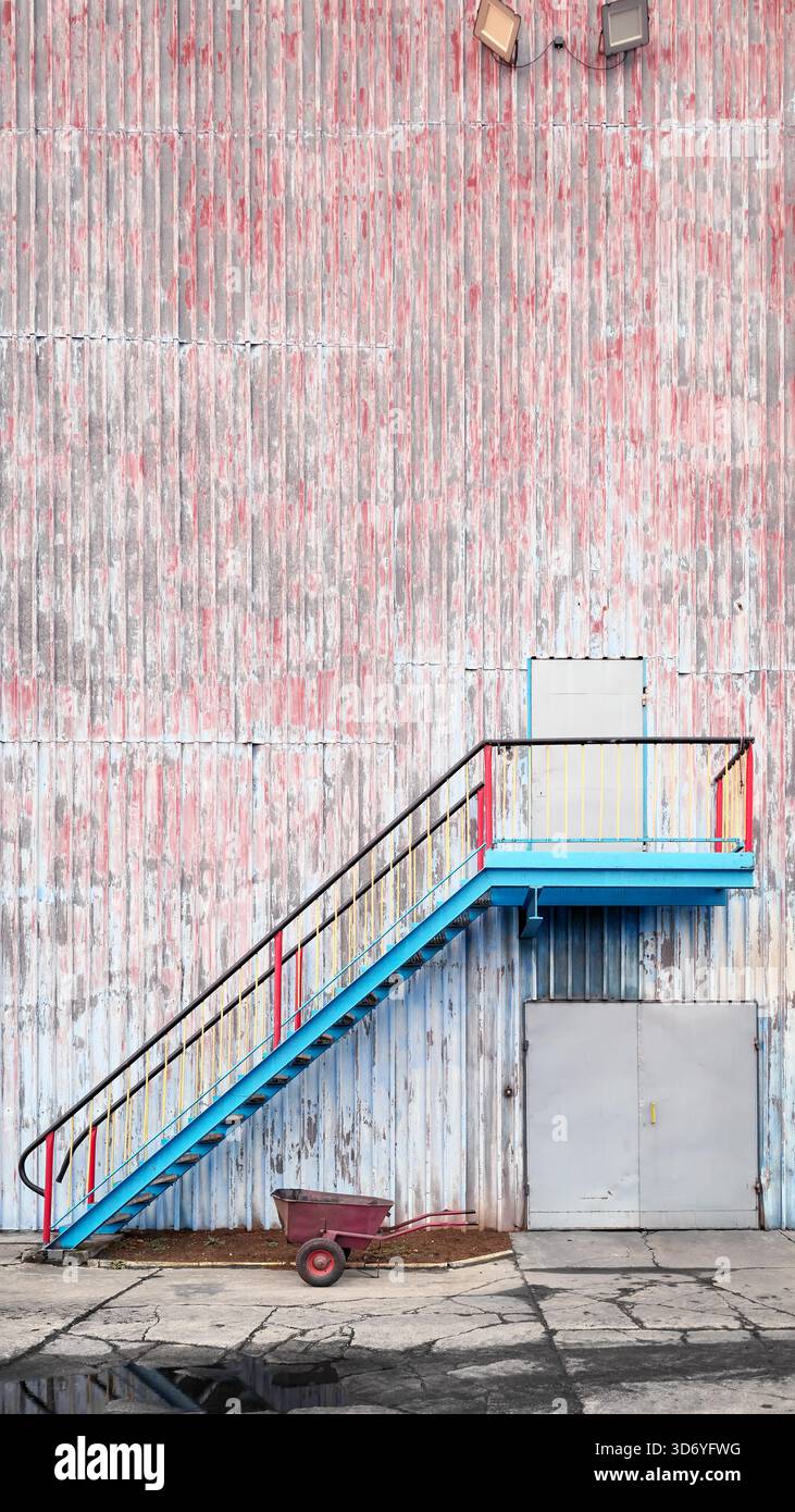 Mur d'un ancien bâtiment industriel avec escaliers et brouette. Banque D'Images