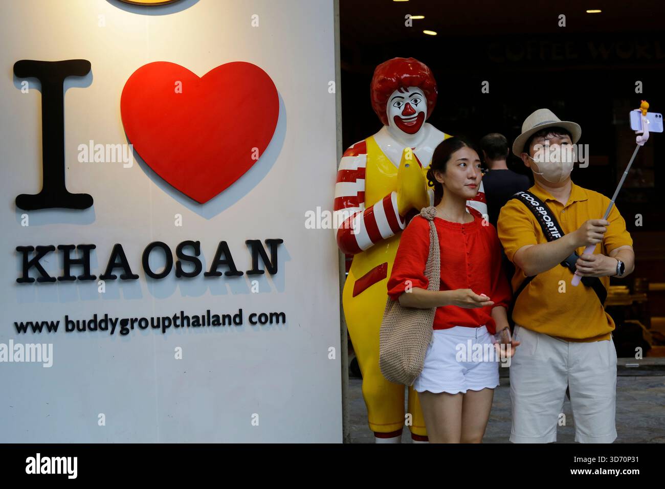 Bangkok, Thaïlande - 22 juillet 2022 : les touristes posent pour des photos à côté d'un mannequin Ronald McDonald faisant un geste à un Wai, ou Namaste, chez un McDonald's.. Banque D'Images